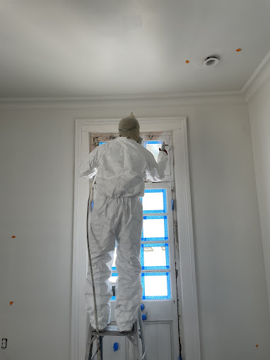 A man in a white coverall painting a window