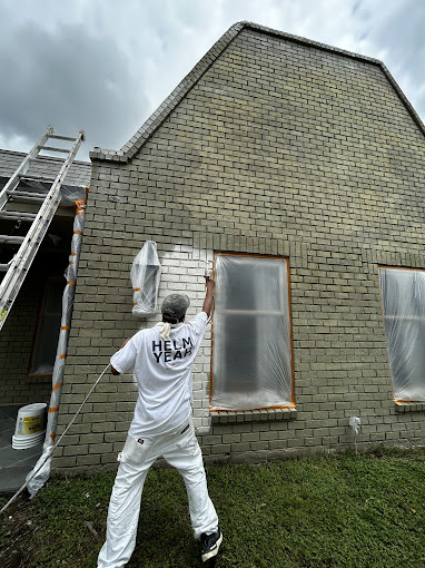 A man painting a brick house with a ladder